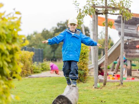 Kindergartenkind balanciert auf Baumstamm im Garten