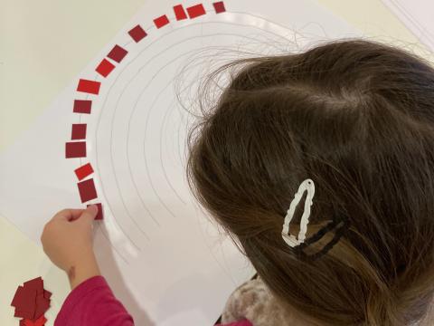 Kind bastelt einen Regenbogen aus Papierschnipseln in der Kita