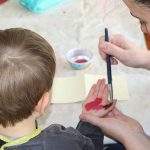 Kinderhand mit Fingerfarbe bepinseln